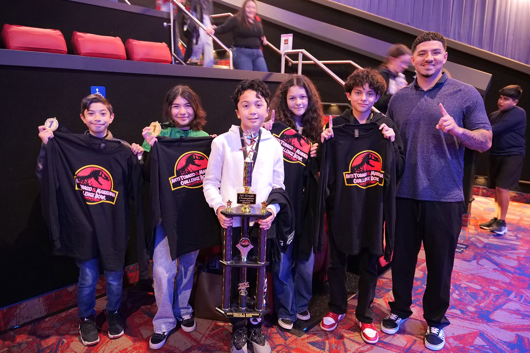3 Students with first place trophy and event shirts in theatre.