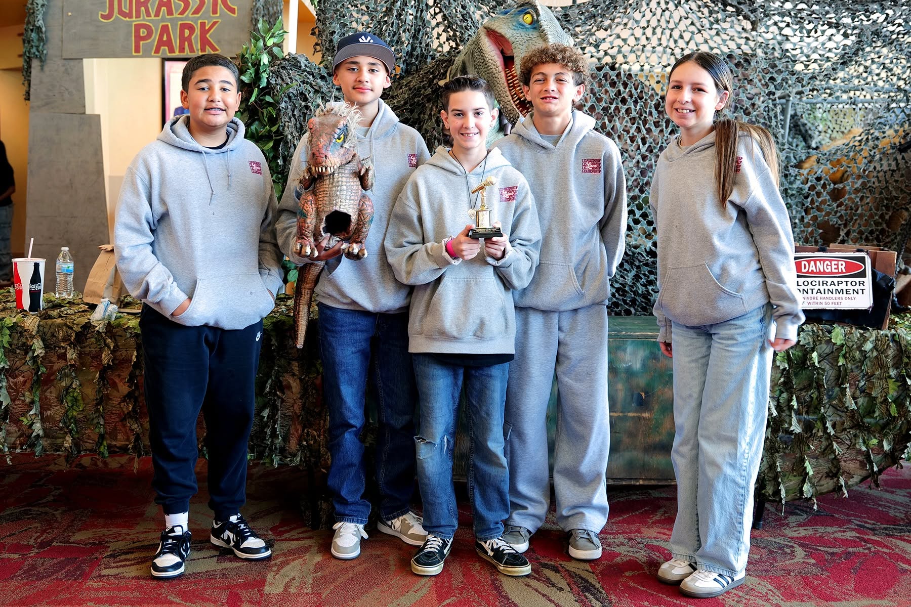 Students with soapbox champion trophy in front of dinosaur backdrop.