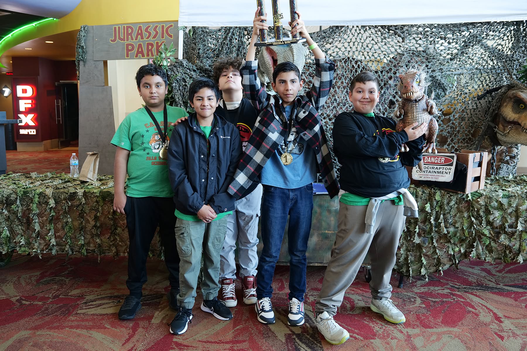 645733112_1540790548054516_9052759054434565900_n Students with a trophy in front of a dinosaur backdrop.